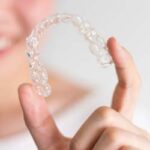 A smiling woman holding invisalign or invisible braces