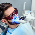 Dentist starting teeth whitening procedure with young man